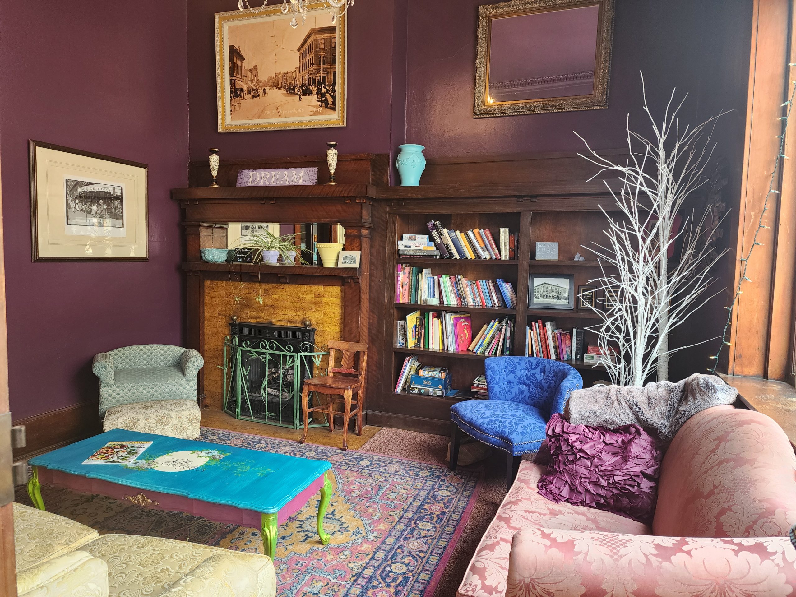 Cozy lounge with bookshelves, a fireplace, colorful seating, and framed wall art.