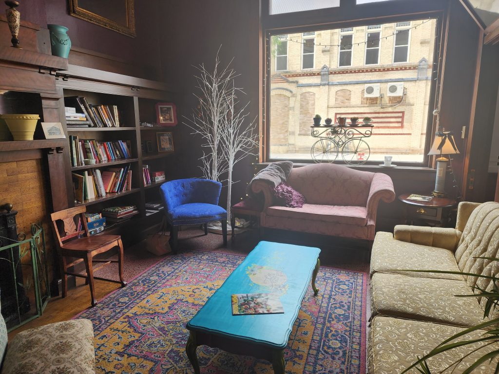 Cozy interior seating area with sofas, chairs, bookshelves, and a large window.