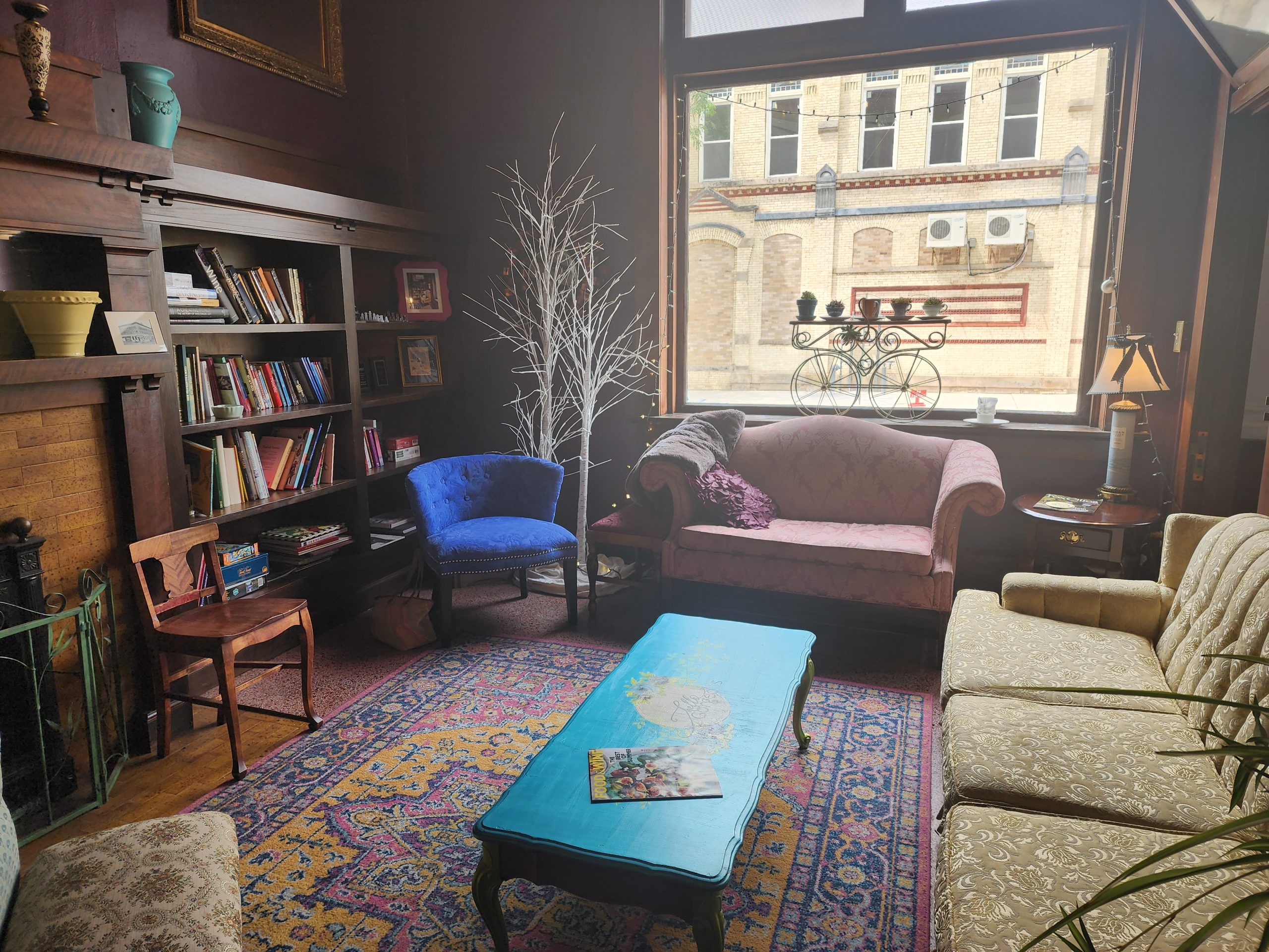 Cozy interior seating area with sofas, chairs, bookshelves, and a large window.