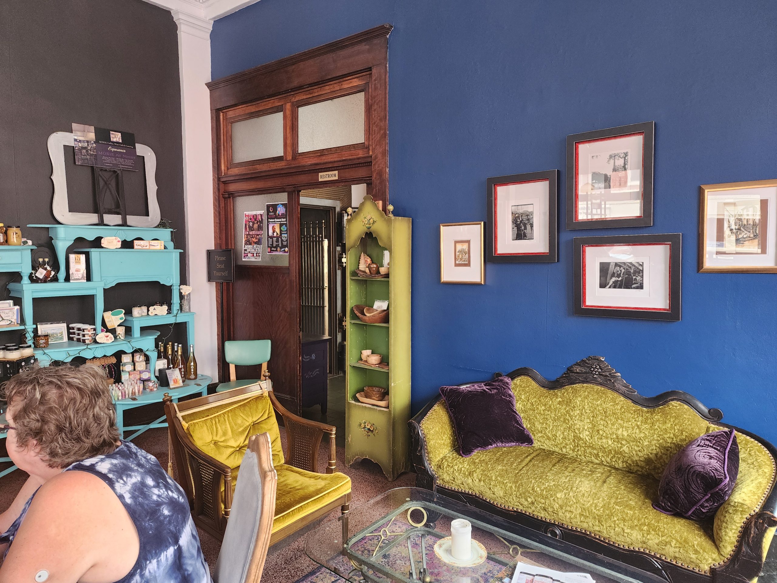 Restaurant interior with vintage seating, framed art, and display shelves.