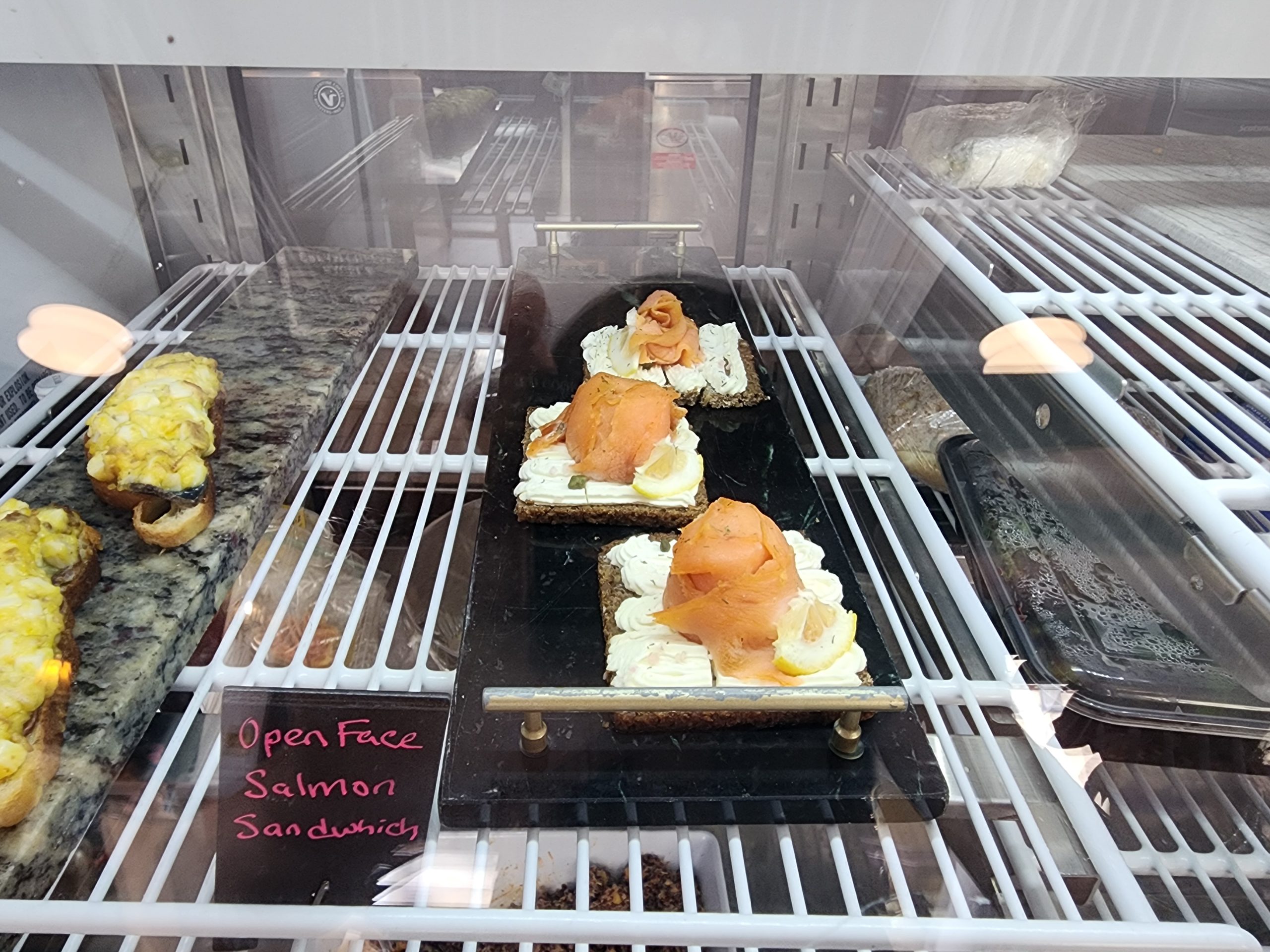 Open-face salmon sandwiches in a glass display case.