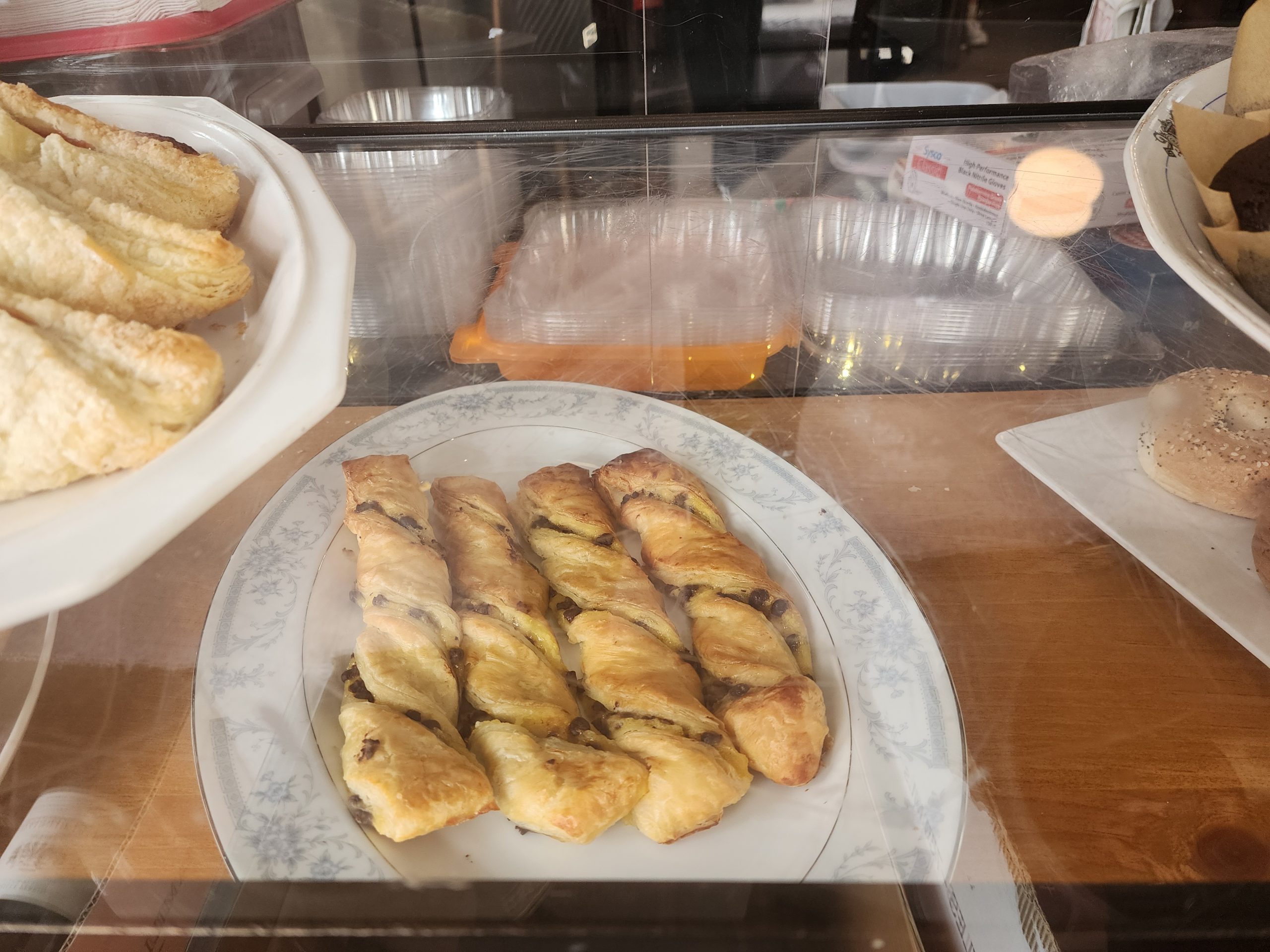 Bakery case with twisted pastries on a plate, croissant-like pastries, and a bagel nearby.