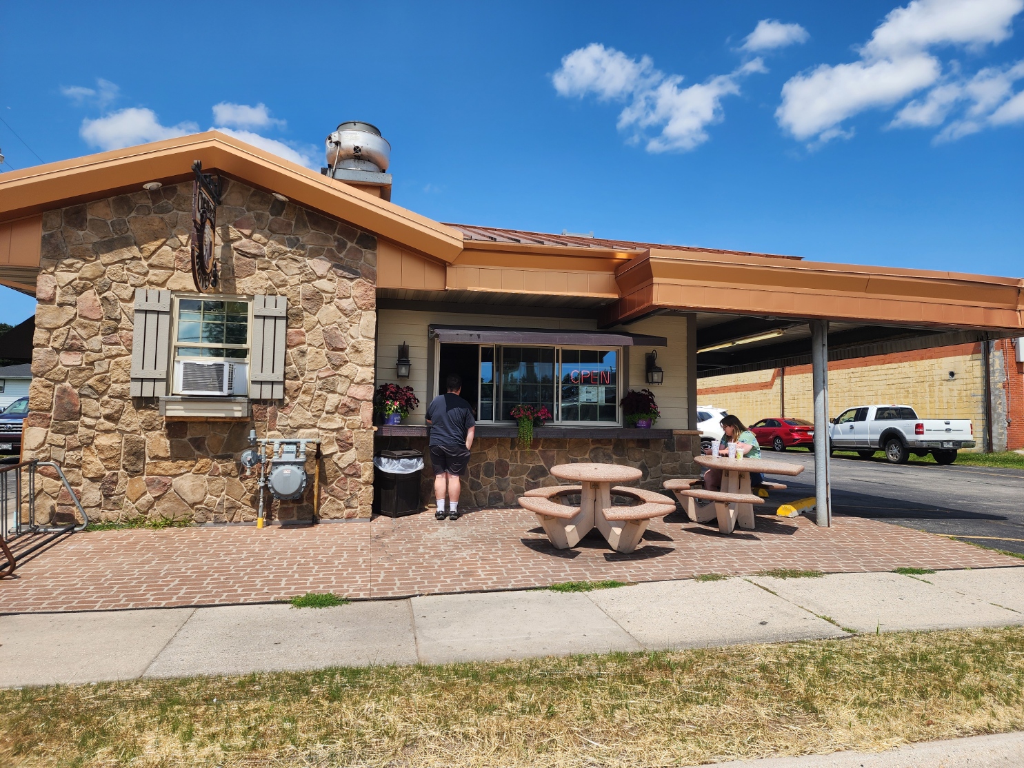 Front exterior of a stone-faced drive-in restaurant with an OPEN sign and outdoor picnic tables.