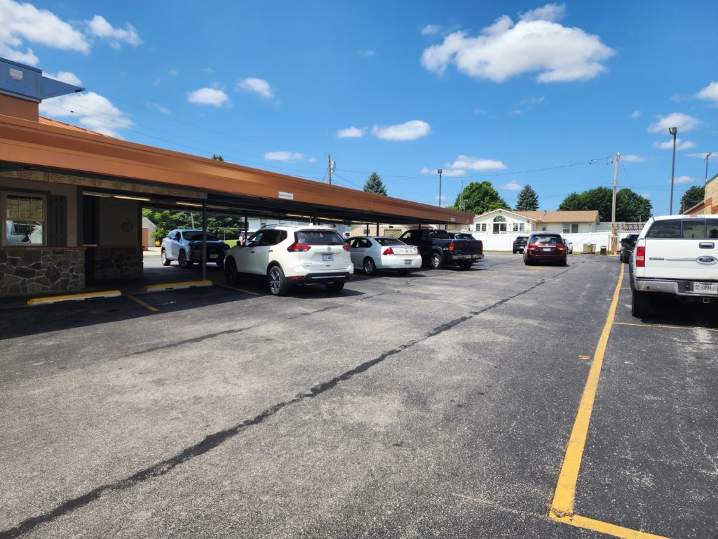 Covered drive-in parking area with several parked vehicles under a bright blue sky.