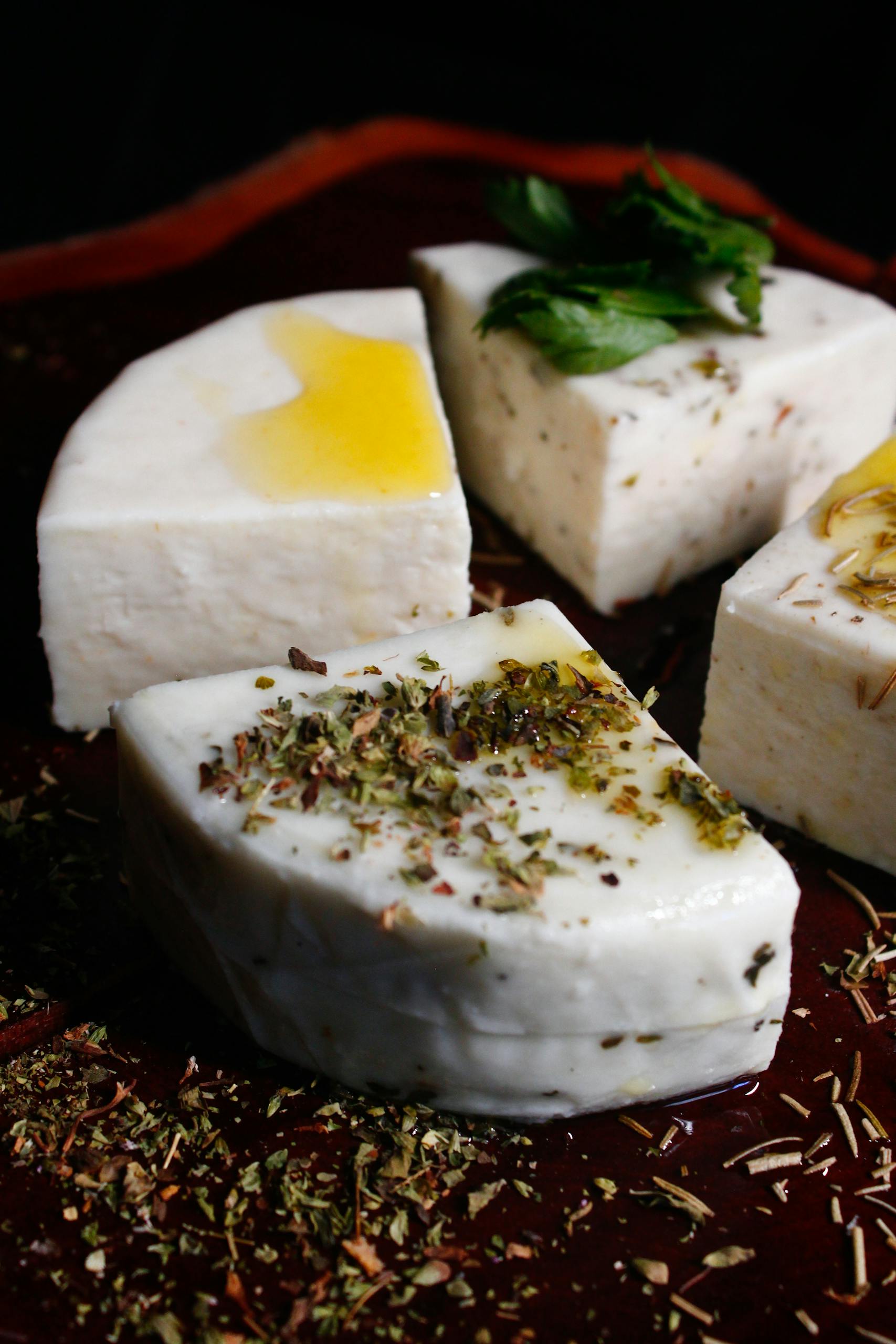 White cheese cubes topped with oil, herbs, and mint leaves.
