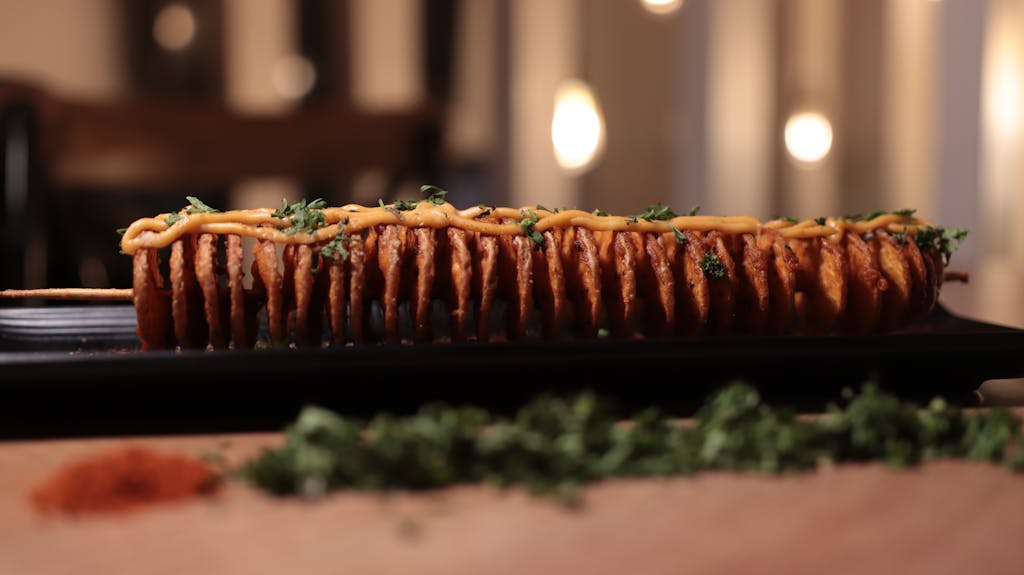 Skewered fried slices topped with sauce and herbs on a serving tray.