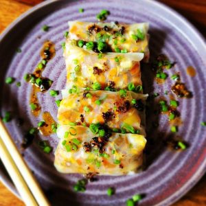 Rice paper dumplings drizzled with chili oil and topped with chopped green onions on a purple plate.