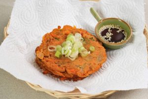 Kimchi pancake topped with sliced green onions on a rattan plate with dipping sauce.