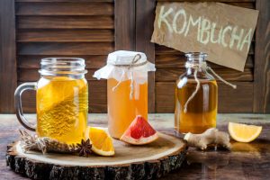 Three jars of kombucha with fruit garnishes on a wooden surface.