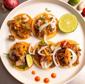 Five pork tacos on a white plate with lime wedges and sliced onion.