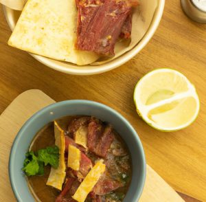 Bowl of bean dip topped with bacon pieces, served with tortilla chips and a lime wedge.