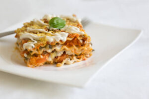 Slice of lasagna topped with basil and creamy sauce on a white plate.