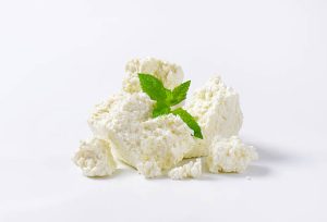 Pieces of ricotta cheese with a green herb garnish on a white background