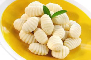 Ricotta gnocchi served on a yellow plate with a green herb garnish.
