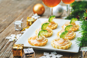 Tartlets topped with salmon mousse, shrimp, and cucumber slices on a serving plate.