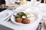 A beautifully plated gourmet meal with crab cakes, salad, and rice on an elegant table setting.