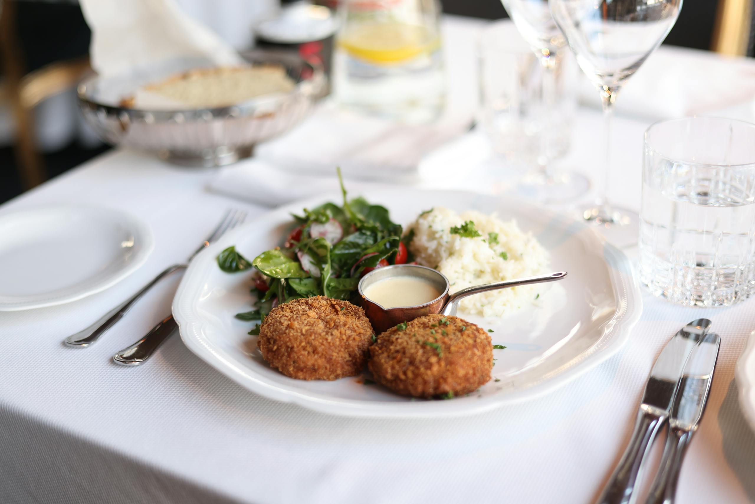 A beautifully plated gourmet meal with crab cakes, salad, and rice on an elegant table setting.
