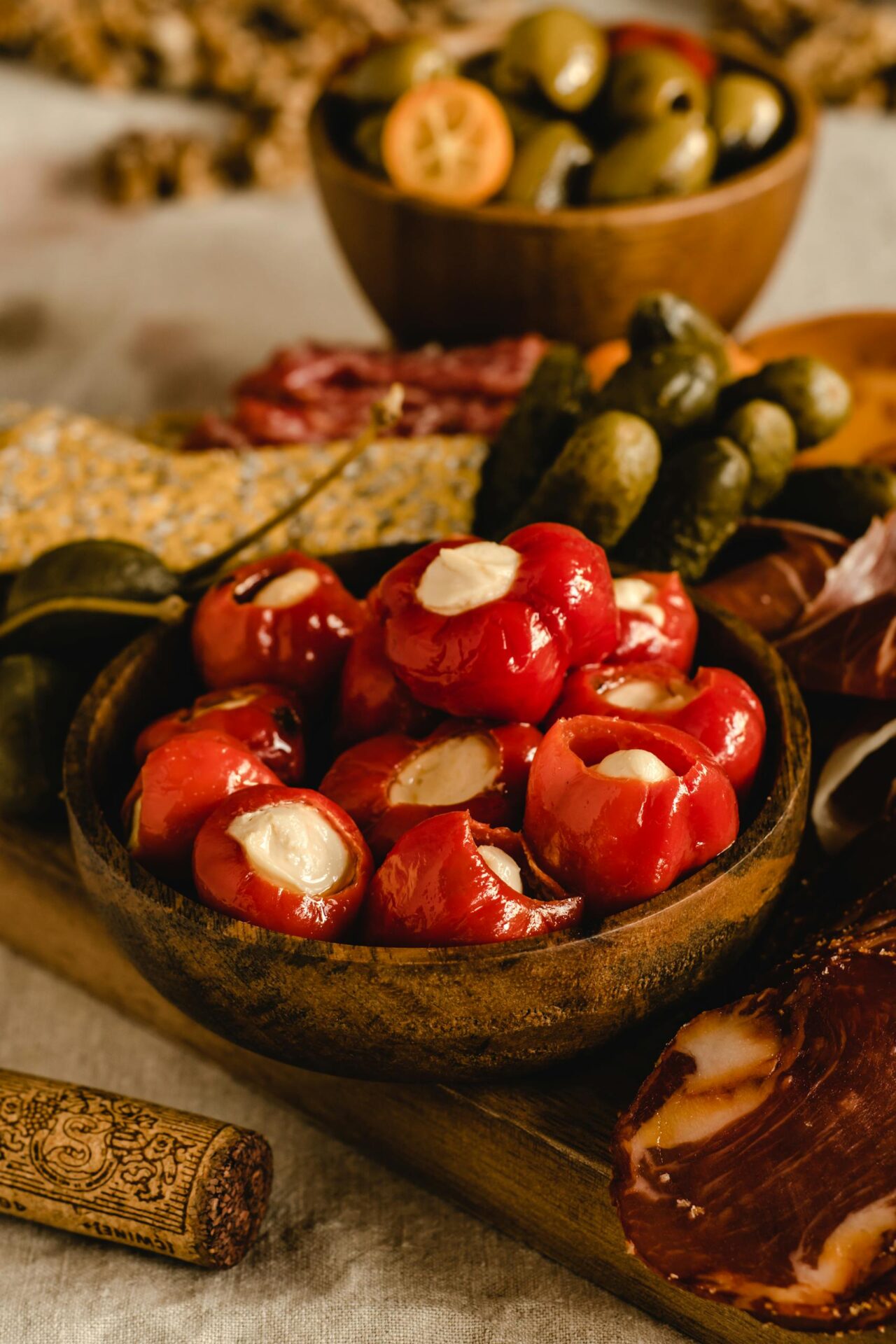 A close-up shot of a rustic antipasto platter featuring stuffed peppers, olives, and cured meats.