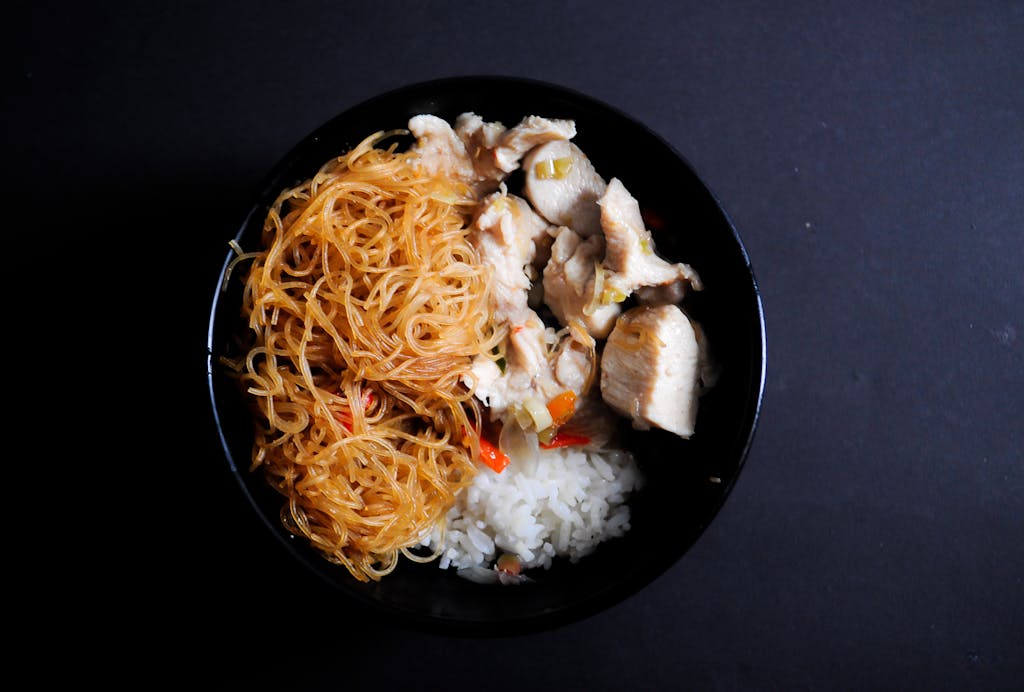 A close-up view of a bowl filled with noodles, rice, and chicken, perfect for a healthy meal.
