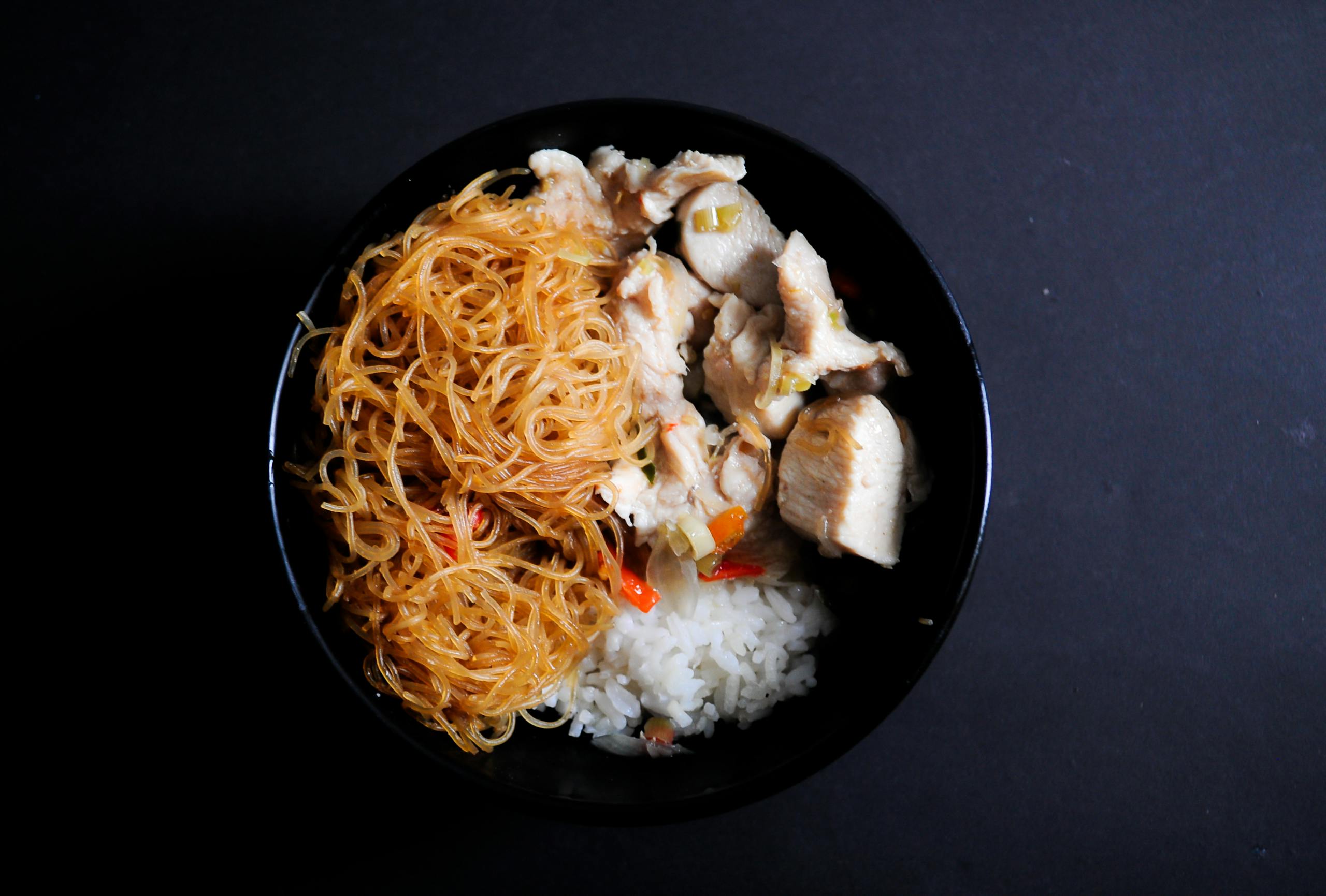 A close-up view of a bowl filled with noodles, rice, and chicken, perfect for a healthy meal.