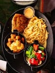 A delectable gourmet meal featuring pasta, breaded cutlet, and fresh vegetables served on a black plate.