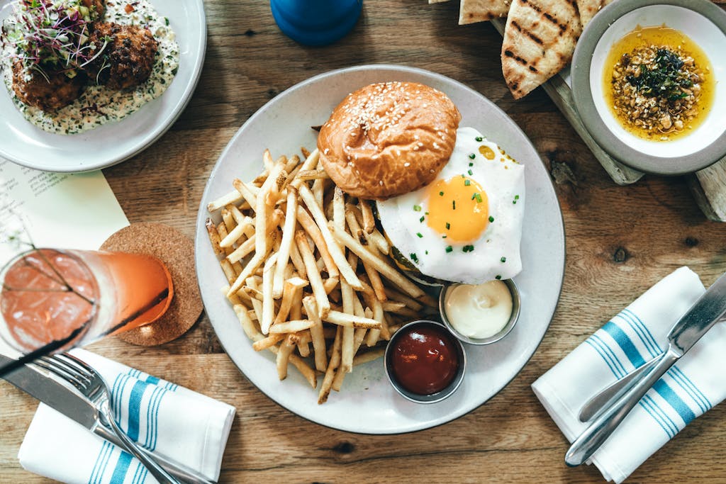 A delicious gourmet burger with fries and a fried egg at a restaurant table.