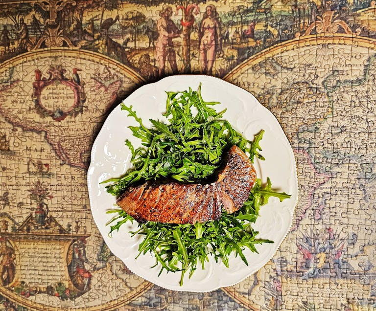 A delicious seared salmon on a bed of fresh arugula served on a vintage map background.
