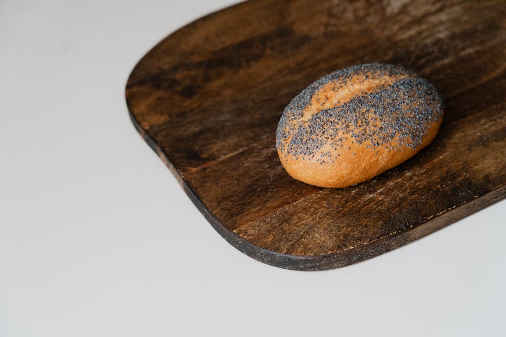 A fresh poppy seed bread roll rests on a rustic wooden cutting board, perfect for culinary themes.