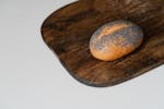A fresh poppy seed bread roll rests on a rustic wooden cutting board, perfect for culinary themes.