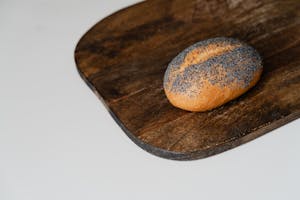 A fresh poppy seed bread roll rests on a rustic wooden cutting board, perfect for culinary themes.