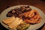 A gourmet beef dinner featuring steak with mushrooms, spaghetti, chips, and guacamole.