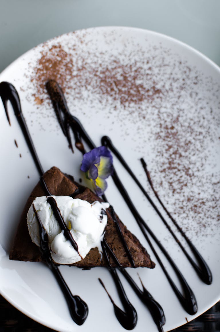A gourmet chocolate dessert slice with whipped cream and edible flower on a ceramic plate, perfect for foodies.