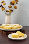 A plate of cornbread slices with a vase of flowers in a cozy setting.