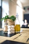 Olive oil bottle, white ceramic salt & pepper shakers, and fresh herbs on a wooden table.