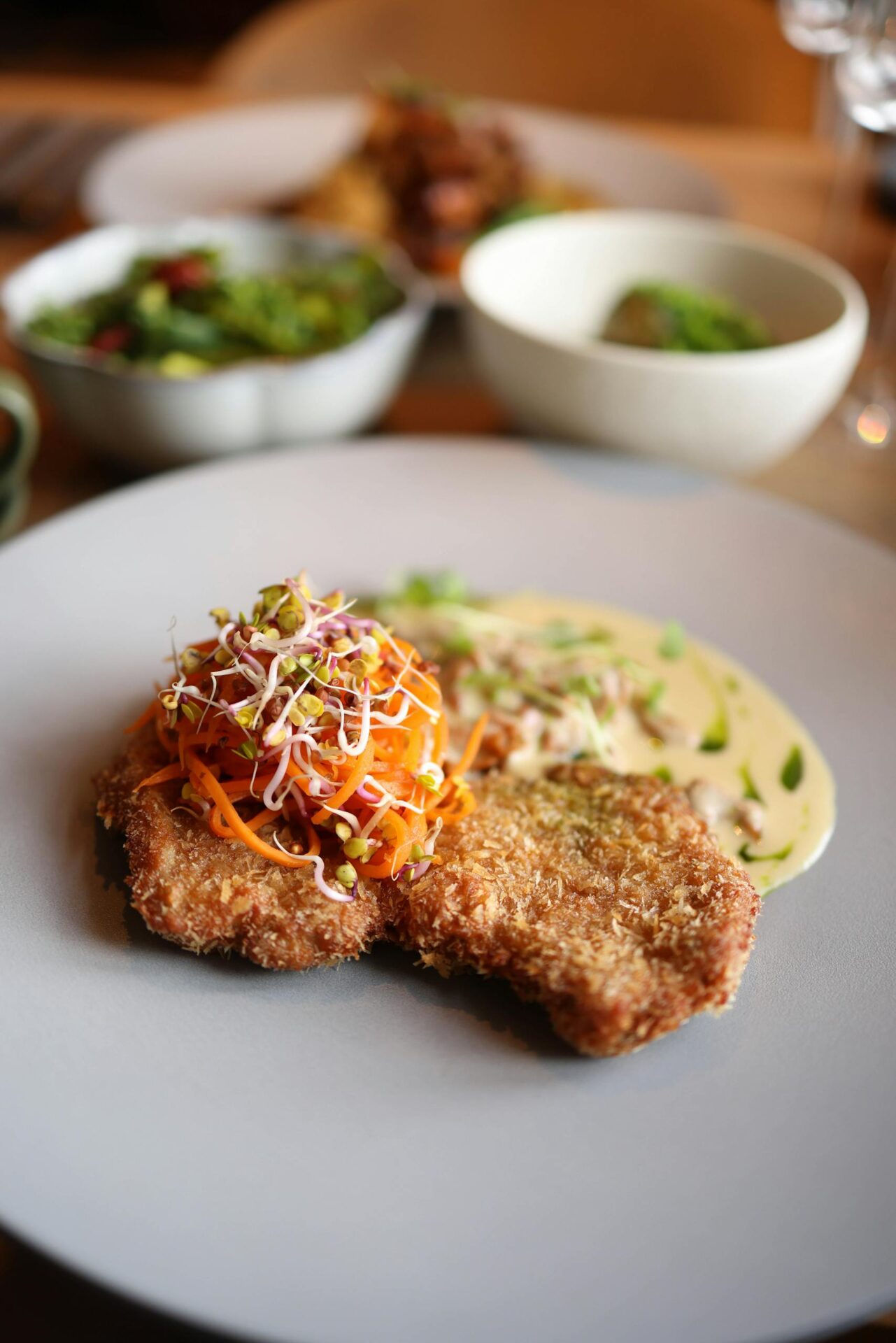 A tasty breaded cutlet topped with fresh sprouts and a creamy sauce on a plate.