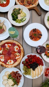A vibrant display of Mediterranean dishes including pizzas, salads, and fruits on a rustic table.