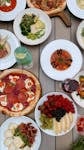 A vibrant display of Mediterranean dishes including pizzas, salads, and fruits on a rustic table.