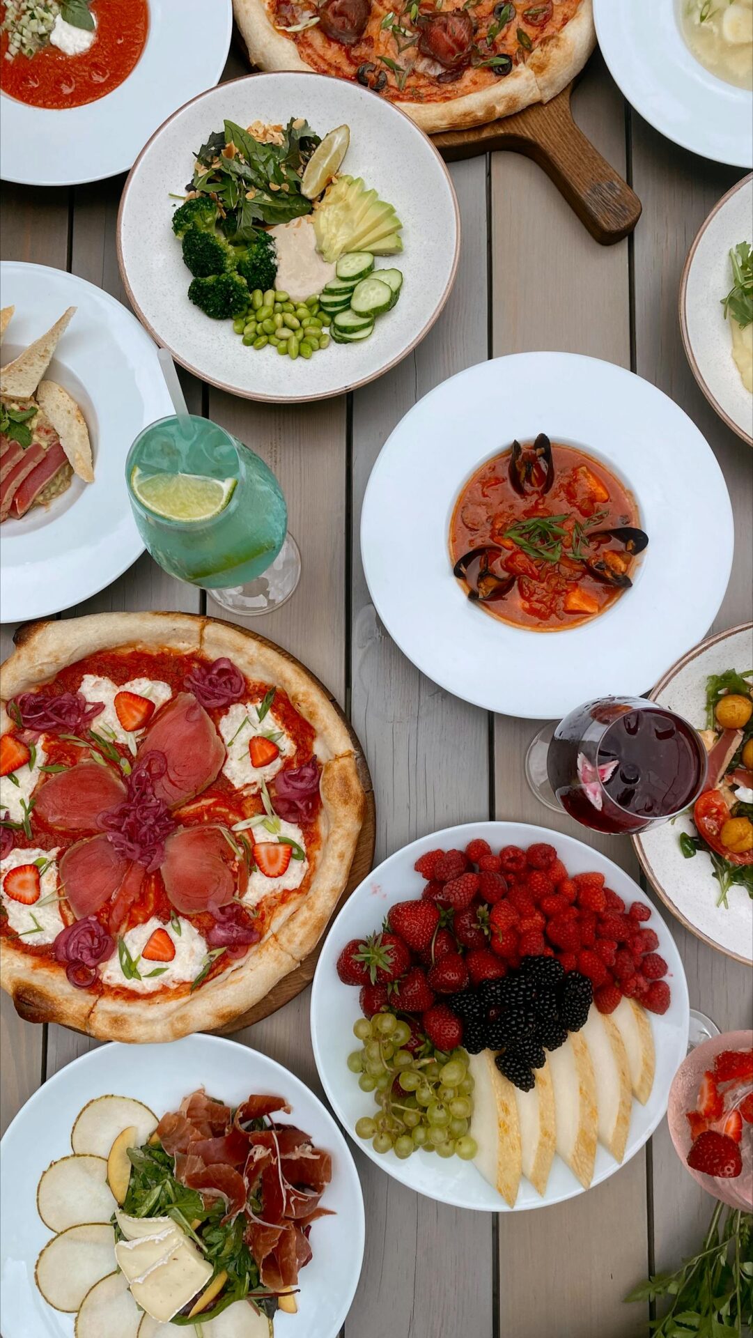 A vibrant display of Mediterranean dishes including pizzas, salads, and fruits on a rustic table.