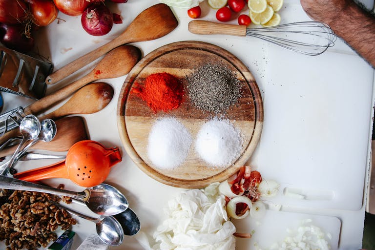 A vibrant flat lay of spices, vegetables, and kitchen tools on a wooden chopping board.