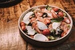 A vibrant fresh salad with smoked salmon, cherry tomatoes, cheese, and greens in a rustic wooden setting.