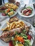 A vibrant Greek meal featuring grilled squid, fresh salad, and fries, perfect for a seafood lover.