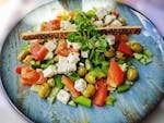 A vibrant salad with feta, olives, tomatoes, and peppers on a blue plate.