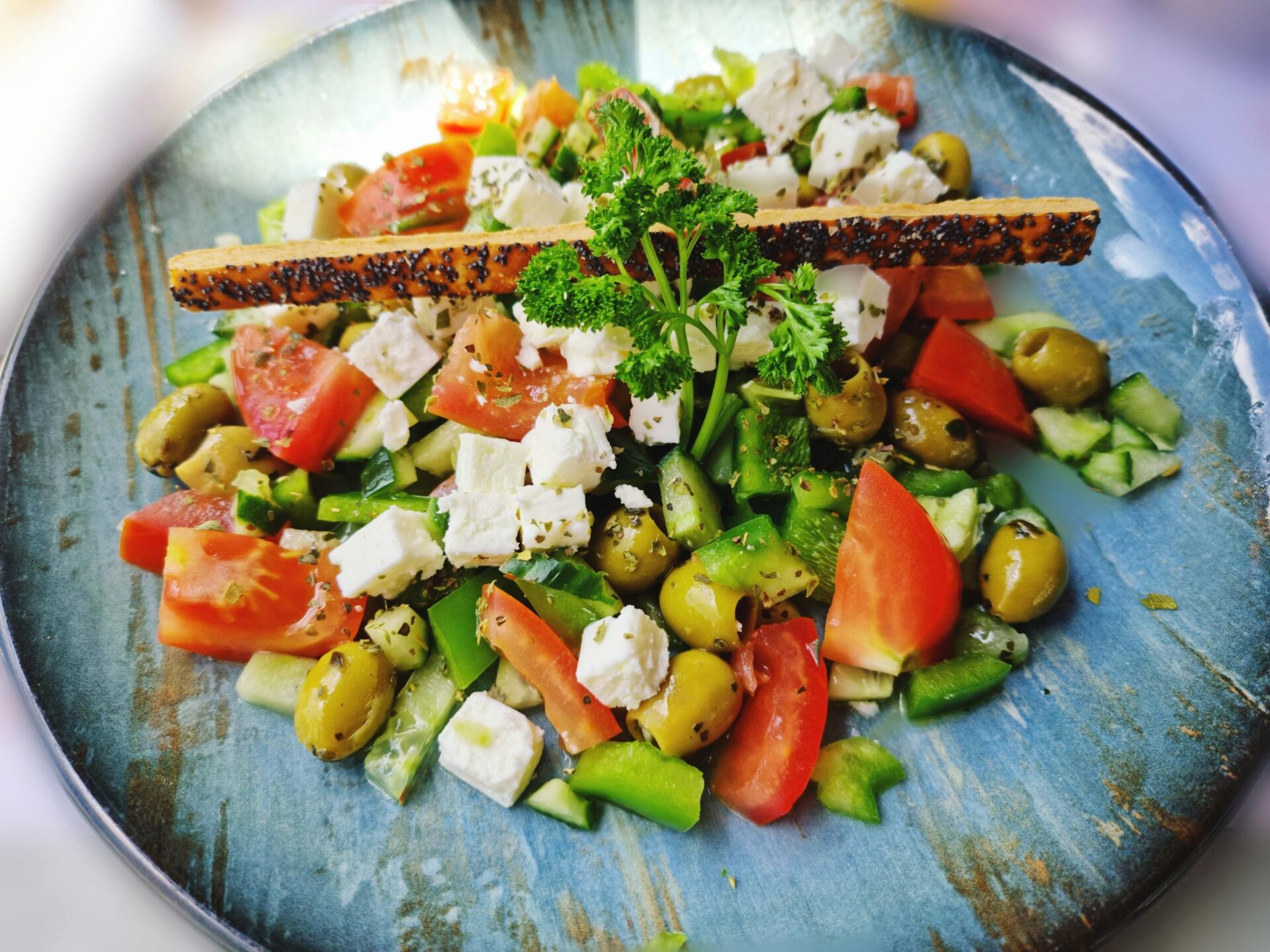 A vibrant salad with feta, olives, tomatoes, and peppers on a blue plate.