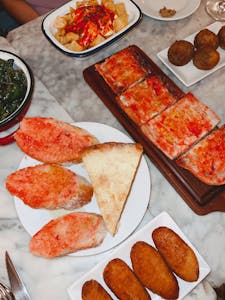 A vibrant spread of Spanish tapas including patatas bravas, bread with tomato, and croquettes on a marble table.