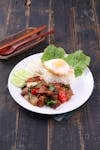 A vibrant Thai dish with basil beef, rice, egg, and fresh vegetables on a rustic table.