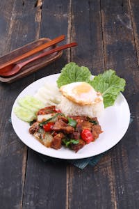 A vibrant Thai dish with basil beef, rice, egg, and fresh vegetables on a rustic table.