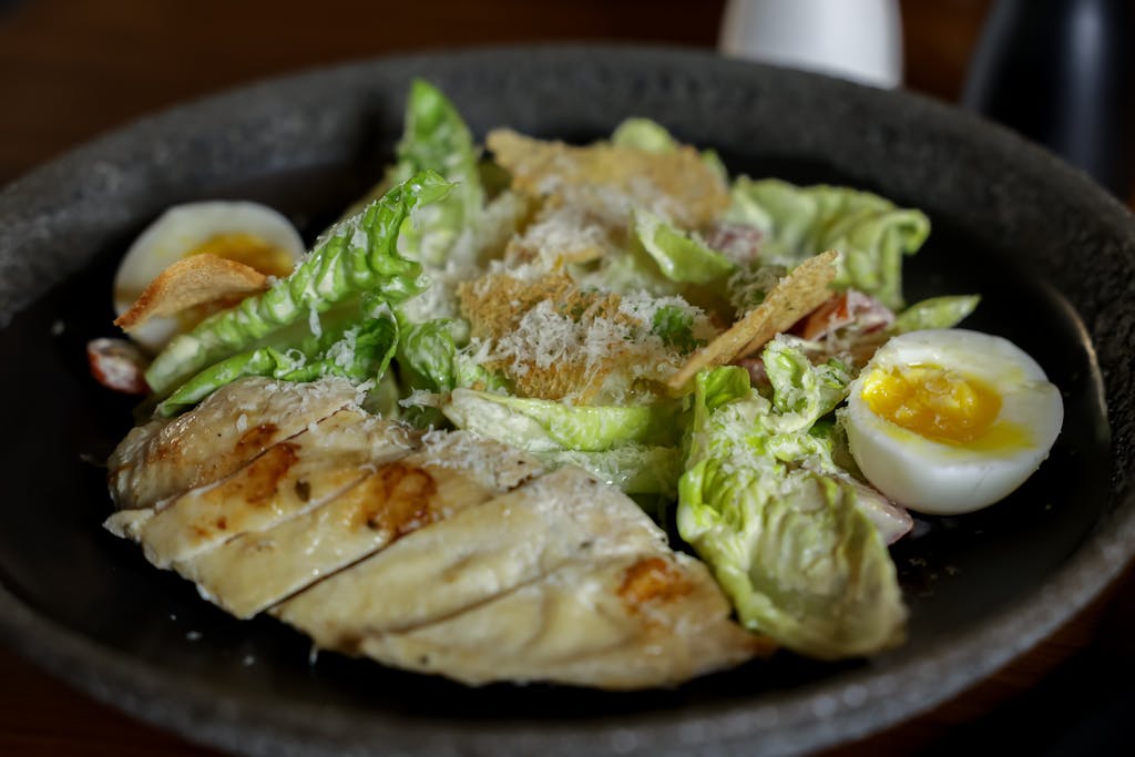 Appetizing Caesar salad with grilled chicken and boiled egg on a black plate.