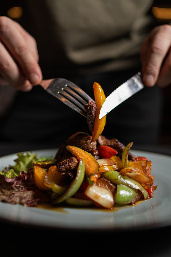 Appetizing steak and vegetables served on a plate with hands using cutlery.