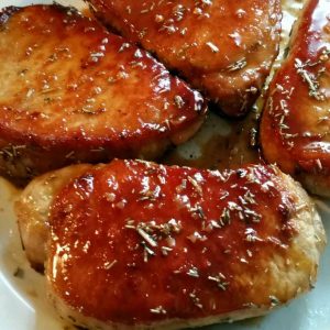 Golden-brown pork chops glazed with a shiny apple cider reduction, served on a white plate with a sprig of rosemary.