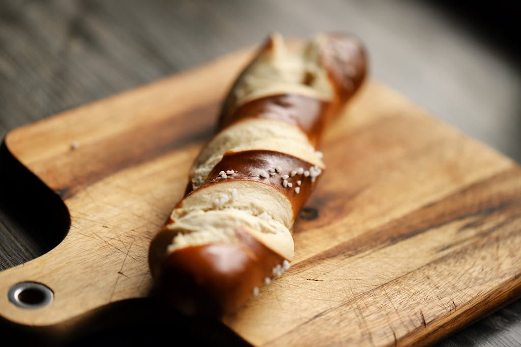 Artistic close-up of a freshly baked pretzel bread loaf on a wooden cutting board with salt atop.